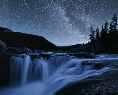 A small waterfall in a forest under a starry night sky